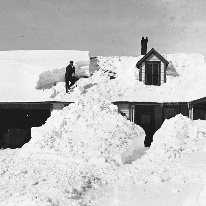 Photograph of man shoveling snow from roof.