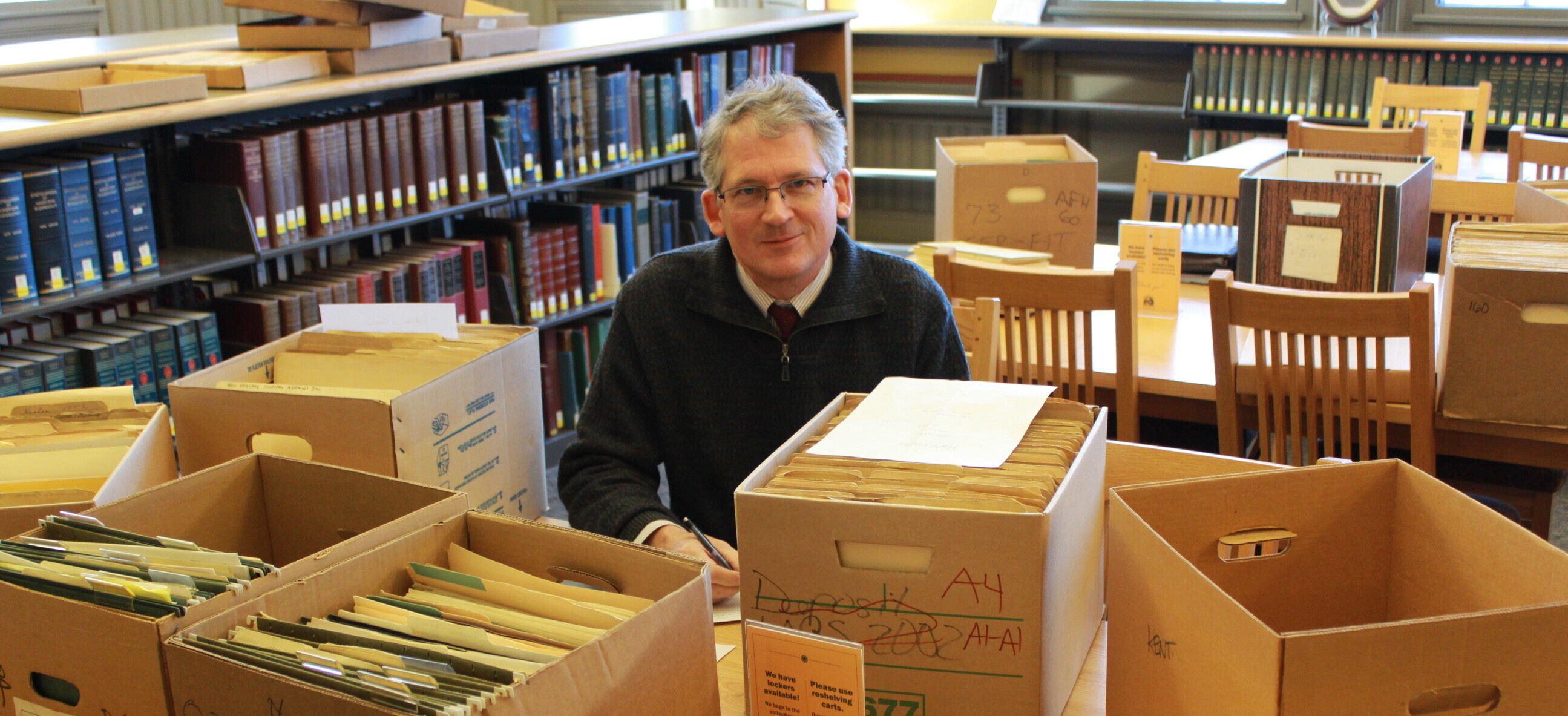 image of Paul Carnahan, VHS Librarian, sitting at a table with boxes of archival materials