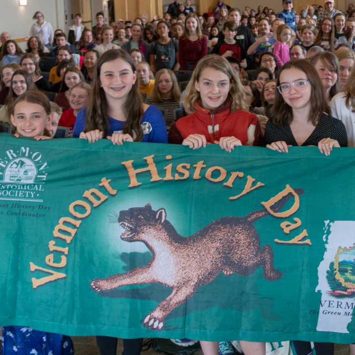 four students holding a Vermont History Day banner in front of a crowd of people