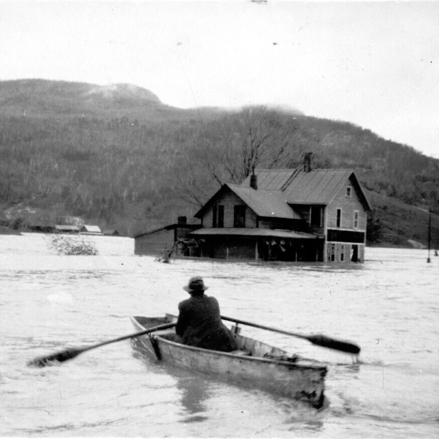 man in rowboat during flood with submerged house in background