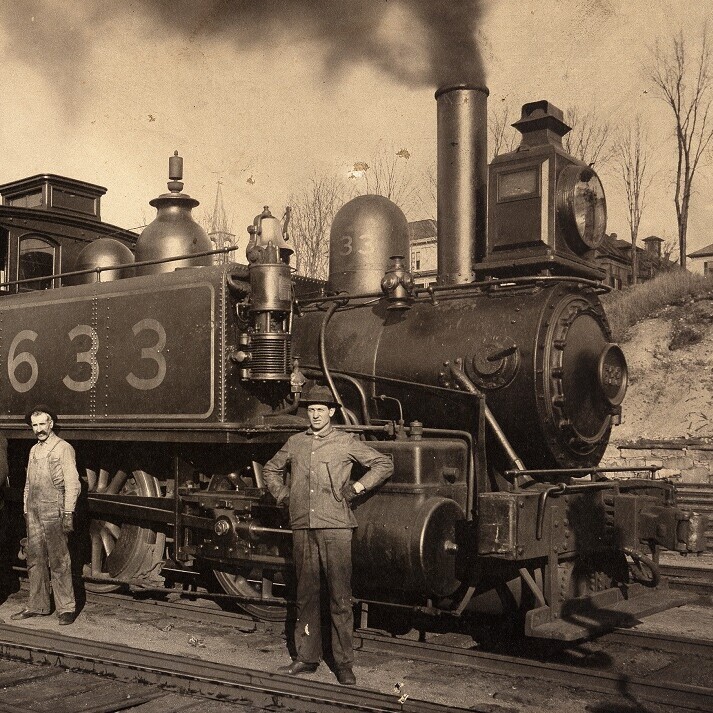 old photo of two men standing in front of locomotive engine