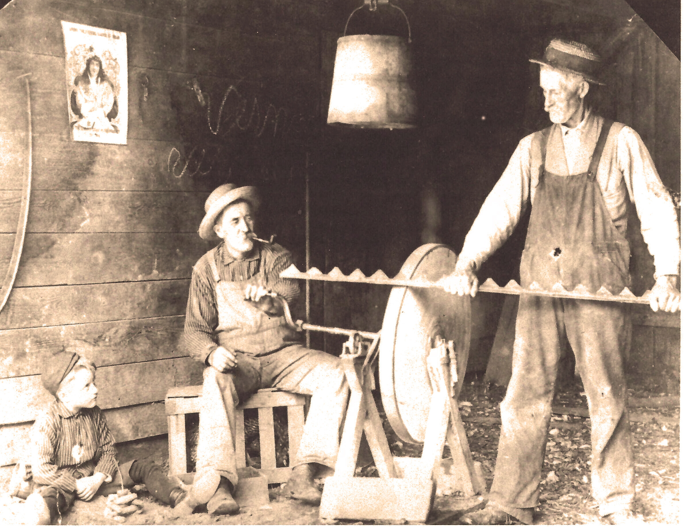 older photo of two older men sharpening a saw while a boy looks on