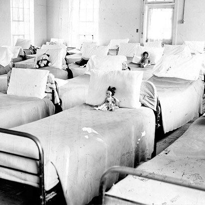 old photo of beds in hospital ward with dolls on them